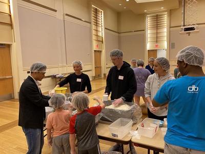 Members of SEAL helping pack food in a small assembly line with some smaller assistants